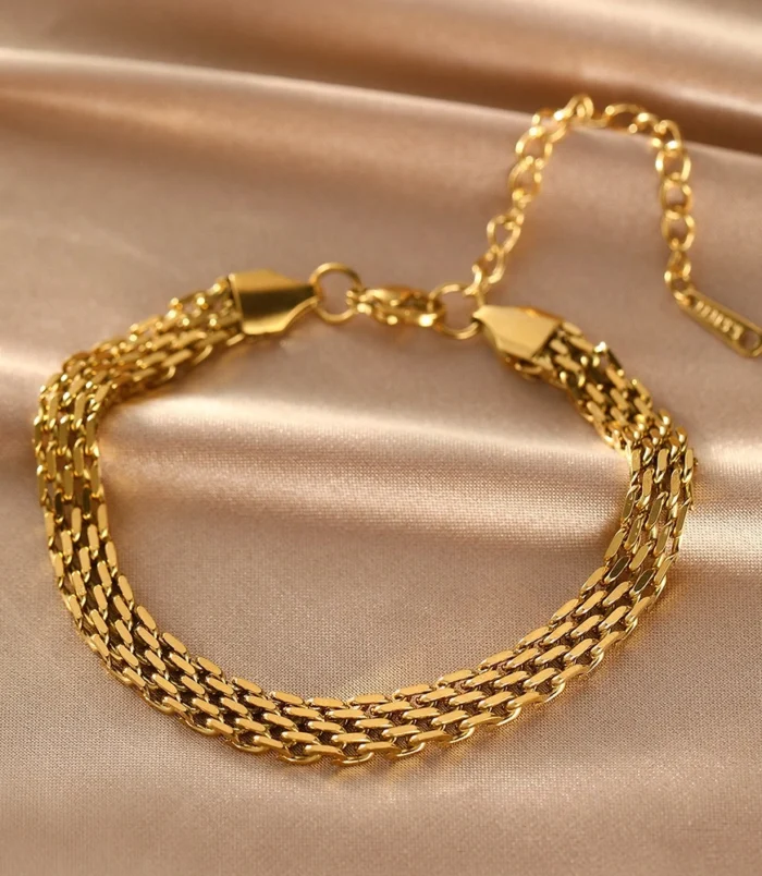 Gold stainless steel chain braided bracelet resting on silk fabric