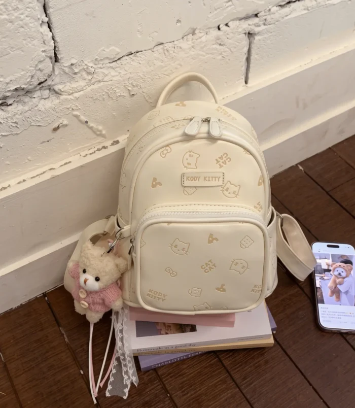 Pastel Cat Print PU Leather Backpack for Women white version resting on books.