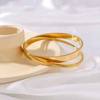 Gold Double Loop Bracelet in Stainless Steel displayed leaning against a small ceramic prop.