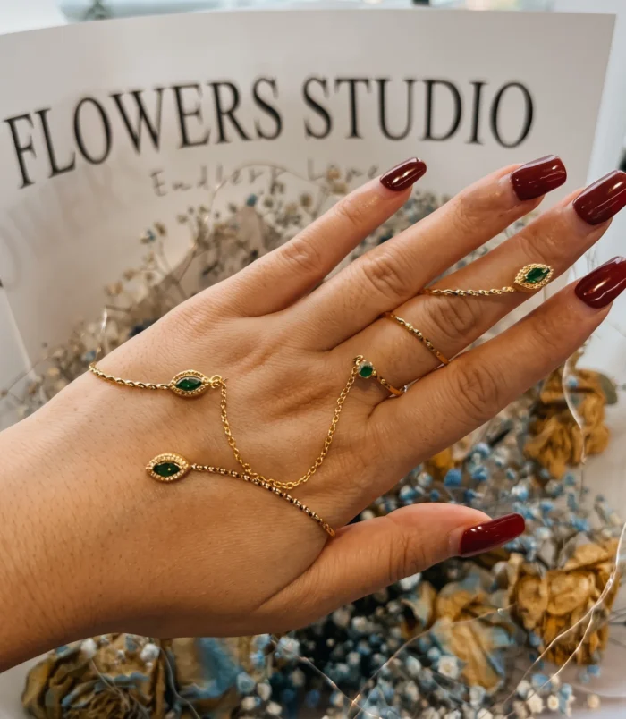 Beautiful rhinestone finger bracelet in gold with green stones worn on hand.