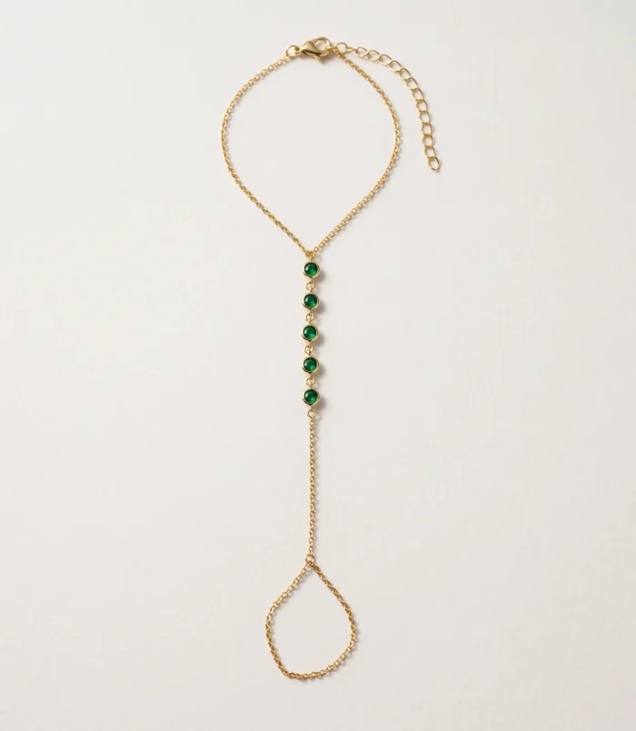 Multicolour rhinestone finger bracelet for women flat lay showing gold plating and green stones.