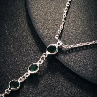 Multicolour rhinestone finger bracelet for women close-up view of the silver connecting chain and green stones.