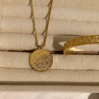 Beautiful gold etched oval necklace resting on a soft display tray.