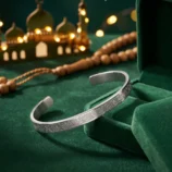 Silver tone stainless steel cuff bracelet displayed with green velvet box and prayer beads.
