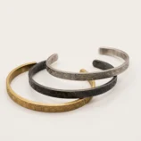 Group view of three stainless steel cuff bracelets in different metallic finishes.